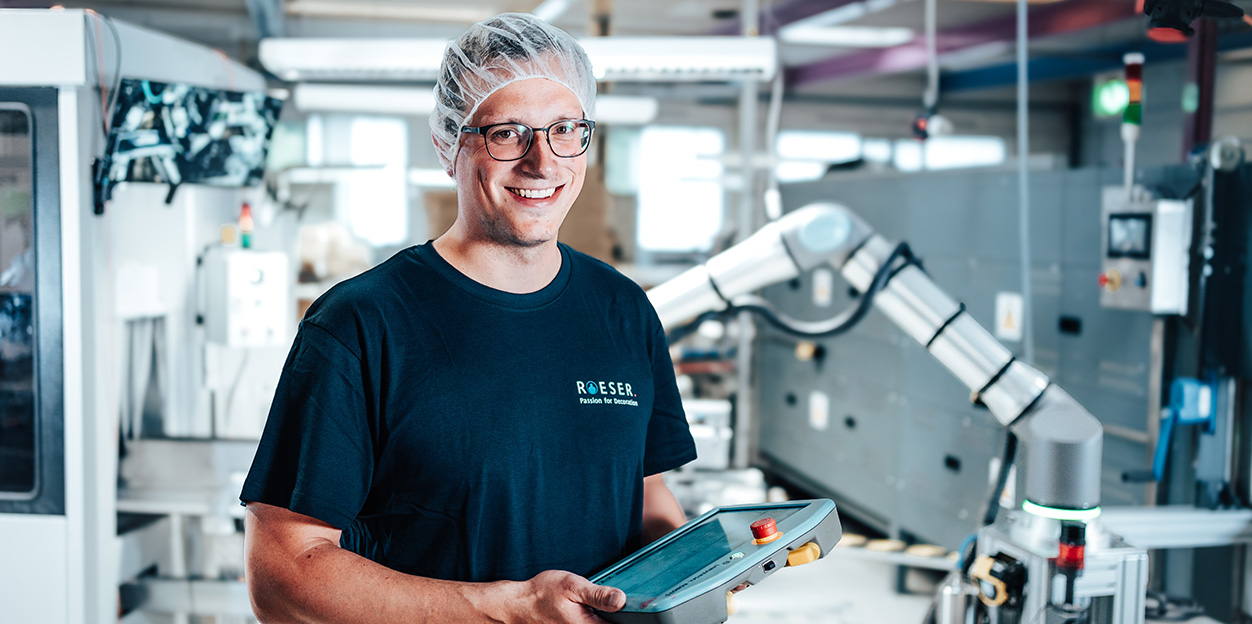 Mitarbeiter lächelt in die Kamera und hält ein Tablet in der Hand