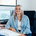 lohn-und-gehaltsbuchhaltung-1 Büromitarbeiterin an einem Schreibtisch lächelt in die Kamera